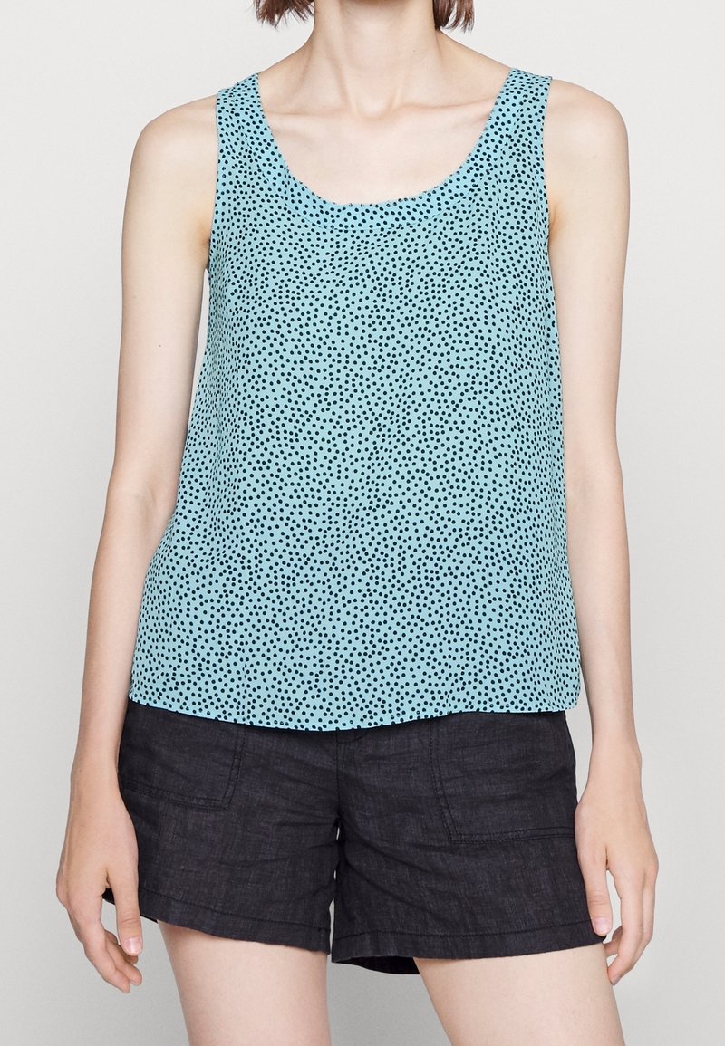 Top senza maniche blu chiaro con pois neri, realizzato in un tessuto liscio, caratterizzato da un colletto rotondo e una vestibilità ampia. Abbinato a pantaloni corti scuri.
