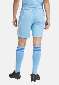 Lichtblauwe sportshorts met roze accenten, gecombineerd met blauwe kniekousen met twee donkerblauwe strepen, en zwarte voetbalschoenen.