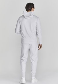 Witte hoodie en bijpassende joggers van een gladde, zachte stof. Heeft een ontspannen pasvorm en ribbels aan de boorden. Sneakers maken de look af.