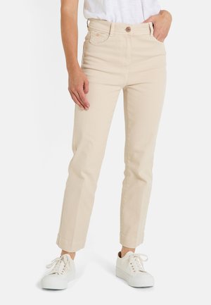 Pantalones de algodón beige de cintura alta con pernera recta, con puños enrollados y cinco bolsillos, combinados con zapatillas blancas.