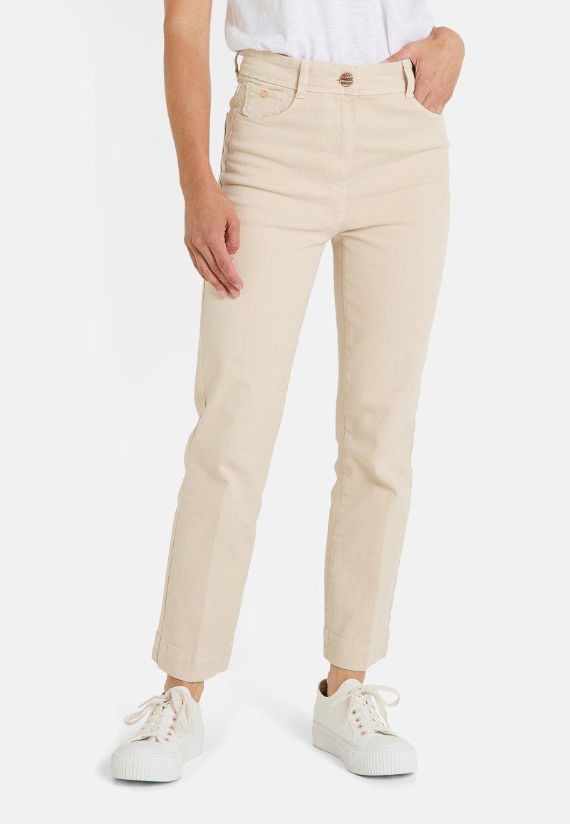 Pantalons en coton beige taille haute avec jambe droite, featuring des revers aux chevilles et cinq poches, associés à des baskets blanches.
