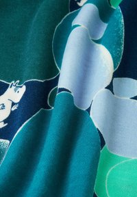 Tissu bleu et vert avec un personnage de dessin animé blanc et de grandes formes ovales bleues et vertes qui se chevauchent.
