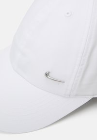 Λευκό καπέλο μπέιζμπολ από μαλακό υλικό, με ασημί logo Nike στο μπροστά μέρος. Ο σχεδιασμός περιλαμβάνει ραμμένα στοιχεία και αεραγωγούς.