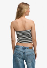 Haut tube ajusté à rayures en tissu noir et blanc, associé à un jean en denim bleu clair taille haute. Sans manches ni bretelles, texture lisse.