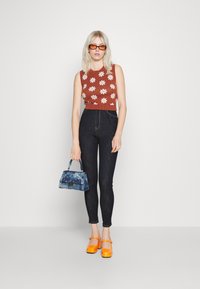 Top cropped florido castanho, jeans skinny de cintura alta escuros, mala de mão em tie-dye azul e sapatos plataforma laranja brilhante.