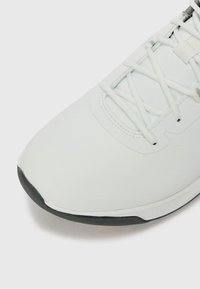 Chaussure de sport blanche avec un upper lisse et texturé, système de laçage et semelle en caoutchouc foncé contrastante. Détails de motif hexagonal subtil.