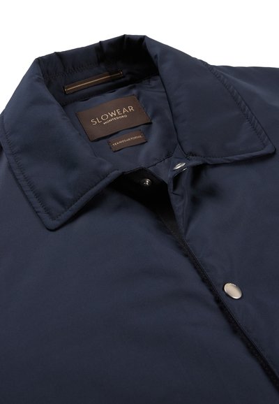 Chaqueta azul marino con cuello y botones de presión, con etiquetas "Slowear Montedoro" y "Teknosartorial" dentro del área del cuello.