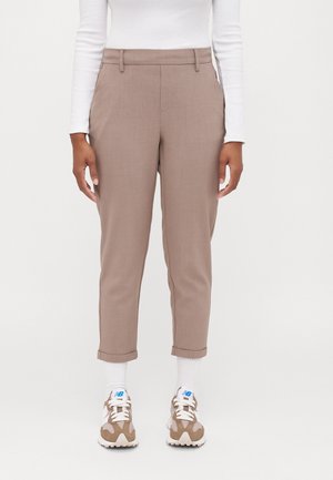 Person iført beige korte bukser, hvid langærmet top, hvide sokker og beige og hvide sneakers med blåt logo.