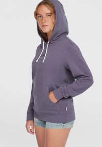 Paarse hoodie met een voorste kangaroozak, witte trekkoorden en geribbelde manchetten. Zachte textuur, casual ontwerp, gedragen met denim shorts.