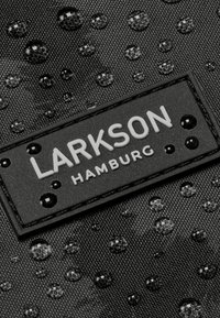 Čierna tkanina s vodnými kvapkami, obsahujúca obdĺžnikovú nálepku s embosovaným nápisom "LARKSON HAMBURG." Textúrovaný povrch s jemným leskom.