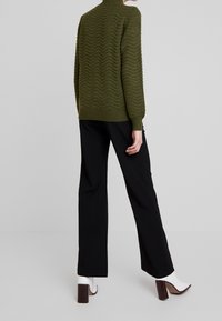 Maglione verde a maglia testurizzata con motivo a onda, abbinato a pantaloni neri a gamba larga e stivaletti bianchi con tacco.