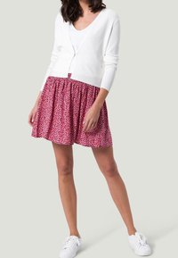 Cárdigan blanco de punto sobre una falda rosa con un patrón floral. Falda fruncida en la cintura, combinada con zapatillas blancas.