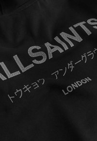 Črn material s tekstom v slogu razpokanega besedila "ALLSAINTS," japonskimi znaki in "LONDON" natisnjenim svetlo sivo.