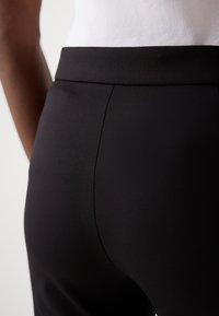 Černé elastické kalhoty z hladké látky s vysokým pasem a přizpůsobeným střihem, zdůrazňující elegantní siluetu.