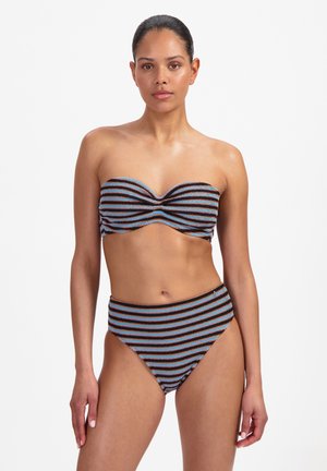 Frau trägt einen trägerlosen, strukturierten Bikini mit horizontalen schwarzen, blauen und braunen Streifen, steht vor weißem Hintergrund und blickt nach vorne.