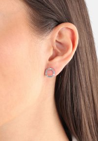 Pendientes en forma de aro circular con un deslumbrante conjunto de piedras multicolores engastadas en una base metálica, que exhiben un diseño de centro abierto.