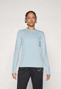 Svetlomodrá dlhá športová košeľa s okrúhlym výstrihom, na hrudi s ružovým logom Nike a športovým, priliehavým strihom.