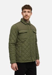 Grøn quilted jakke med trykknapfront, to brystlommer og krave. Har en glat tekstur og en let tætsiddende design.