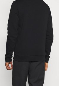 Felpa nera con scollo rotondo, polsini e orlo ribattuti, realizzata in materiale morbido, caratterizzata da un design pulito e minimal. Vista posteriore mostrata.