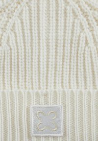Witte gebreide beanie met ribbelstructuur, zachte garen en een vierkante patch met een geborduurd decoratief ontwerp in beige.