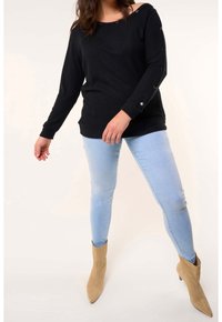 Haut noir à rayures, à manches longues, avec un design décolleté et des accents de boutons. Associé à un jean skinny bleu clair et des bottines à bouts pointus beiges.