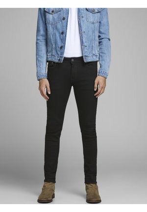 Jean skinny noir avec une texture lisse, doté d'une fermeture à bouton et à glissière à l'avant, associé à une veste en denim bleu clair.