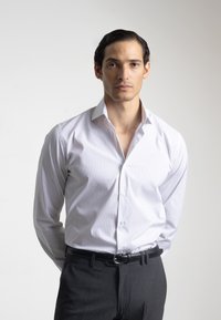 Camisa blanca de vestir con finas rayas verticales, cuello abotonado y mangas largas, combinada con pantalones oscuros y un cinturón negro.