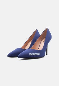 Ζευγάρι σκούρα μπλε ψηλοτάκουνα παπούτσια με μυτερή μύτη, με την επιγραφή «LOVE MOSCHINO» σε λευκά γράμματα στη εξωτερική πλευρά του αριστερού παπουτσιού.