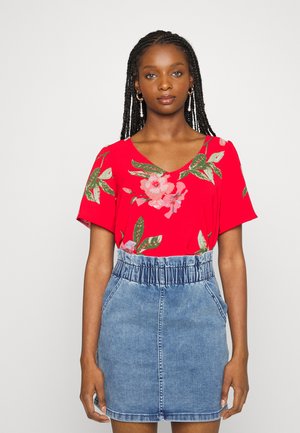 Blusa floral vermelha de mangas curtas, combinada com uma saia de denim azul claro com cintura elástica e bolsos.
