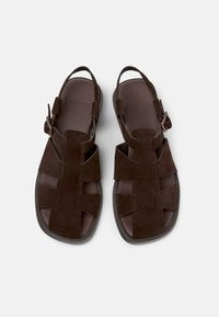 Sandalias de ante marrón con suela plana, con diseño de tiras cruzadas y hebilla ajustable en el talón para un ajuste seguro.