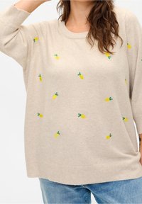 Pullover beige chiaro con ricami di ananas gialli e dettagli verdi. Texture morbida, vestibilità comoda e maniche lunghe tre quarti.