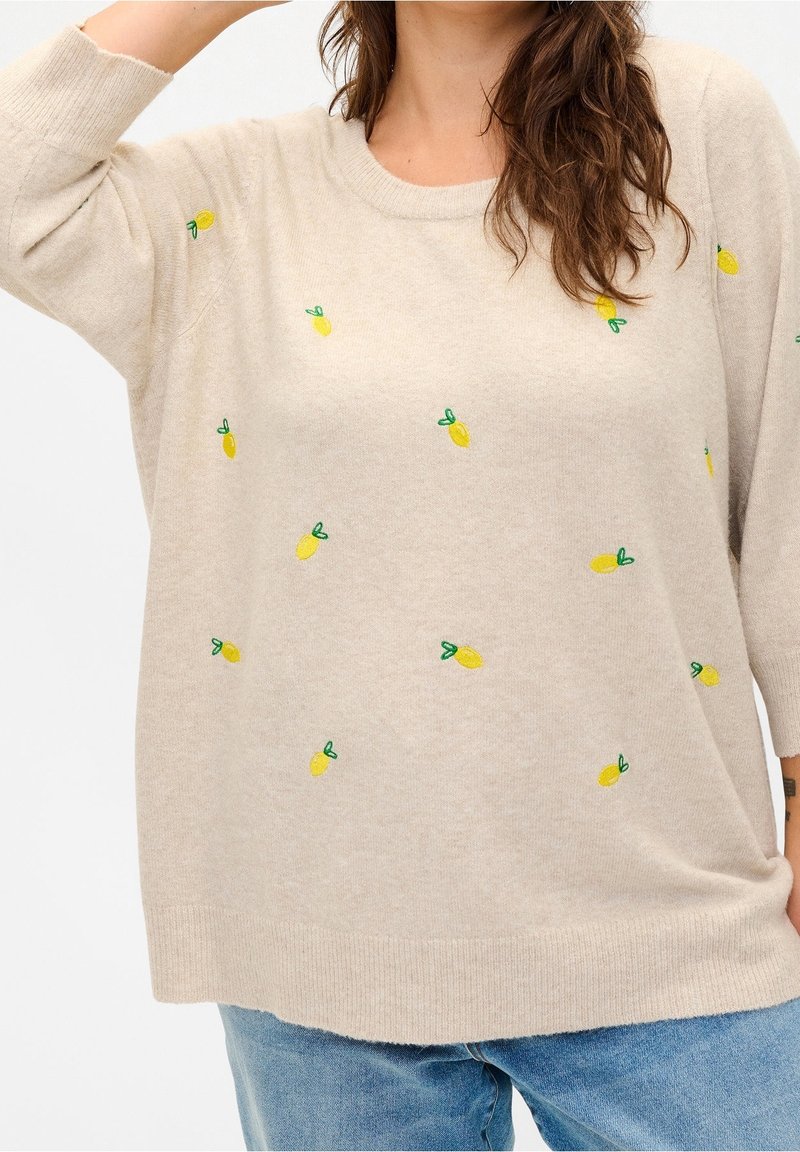 Pullover beige chiaro con ricami di ananas gialli e dettagli verdi. Texture morbida, vestibilità comoda e maniche lunghe tre quarti.