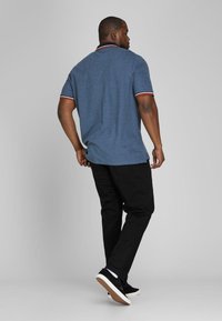 Blue polo shirt with contrasting red and white trim on the collar and sleeves, paired with black pants and black sneakers, viewed from behind.