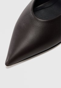 Zapato de cuero negro de punta puntiaguda con textura lisa y diseño recortado. El forro interior es de color oscuro contrastante.