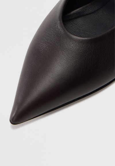 Μαύρο δερμάτινο παπούτσι με μυτερή μύτη, με λεία υφή και σχέδιο με ανοίγματα. Η εσωτερική επένδυση είναι σε αντίθετο σκούρο χρώμα.