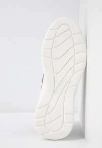 Semelle de chaussure en caoutchouc blanc avec des motifs incurvés, photographiée sur un fond blanc avec angles.