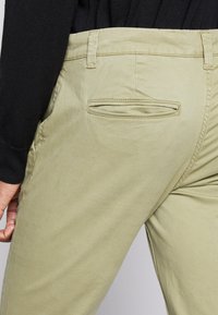 Light green cotton twill chinos with a back pocket, plain texture, and stitched seams. Paired with a black textured sweater sleeve.