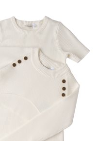 Dwa swetry w kolorze kremowym z prążkowanej tkaniny ułożone jeden na drugim. Jeden z nich ma okrągły dekolt i brązowe guziki na ramieniu, podczas gdy drugi ma gładkie wykończenie.