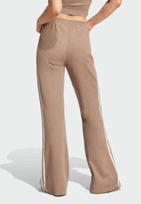 Beige utsvängda byxor i en strukturerad tygkvalitet, med vita sidostraper och ett elastiskt midjeband. Designen är smidig och avslappnad.