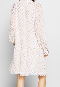 Robe florale blanche à manches longues, présentant une taille froncée, une bordure en dentelle à l'ourlet, et de petits motifs floraux colorés sur l'ensemble.