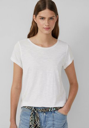 T-shirt blanc à manches courtes en tissu léger et texturé, avec un col arrondi. Associé à un short en denim avec une ceinture à motifs.