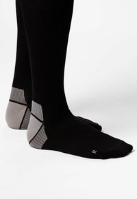 Black compression socks with a textured gray heel and arch support. They feature solid color and a sleek, fitted design.