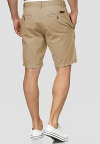 Khaki shorts made of cotton, featuring a straight cut, two back pockets with buttons, and a belt loop at the waist.