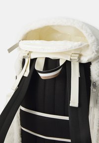 White fleece-lined backpack with a smooth inner lining and black mesh straps. Features adjustable straps and metal hardware accents.