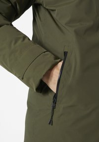 Giacca verde oliva con tessuto testurizzato, dotata di una tasca laterale con zip e polsini regolabili, che mostra un design elegante e moderno.