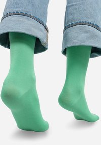 Widać zielone bawełniane skarpetki, zestawione z podwiniętymi niebieskimi dżinsami. Skarpetki mają gładką fakturę i jednolity kolor.