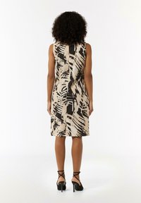 Ärmelloses Kleid aus beigem Stoff mit einem abstrakten Blattmuster in Schwarz und Creme. Es hat eine figurbetonte Silhouette und einen knielangen Saum.