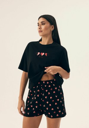 Czarny bawełniany t-shirt z krótkim rękawem, z różowym wzorem serca, w zestawie z czarnymi szortami ozdobionymi małymi czerwonymi sercami.