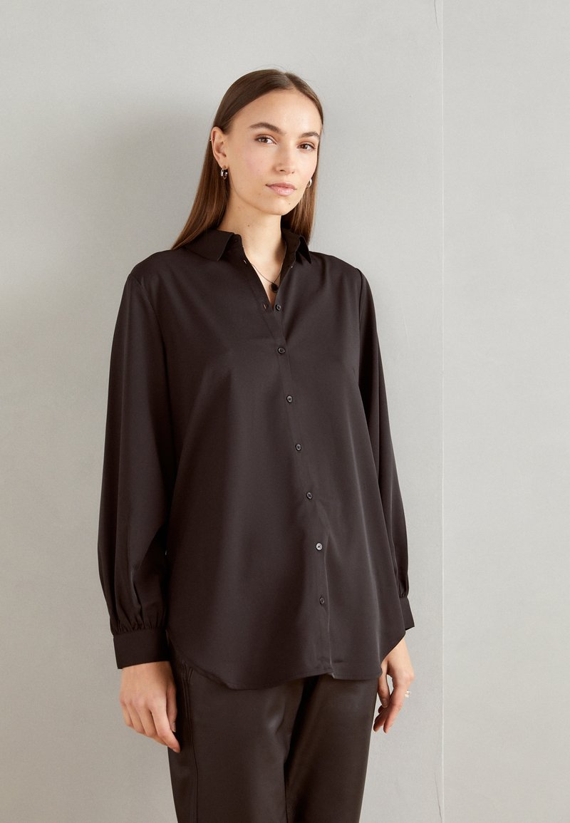 Black long-sleeve shirt made of smooth fabric, featuring a classic collar, button-down front, and relaxed fit with gathered cuffs.