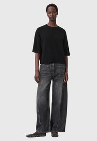 Maglione nero lavorato a maglia a maniche corte, abbinato a jeans larghi grigi scuri con tasche laterali. Scarpe nere a pianta bassa con borchie.